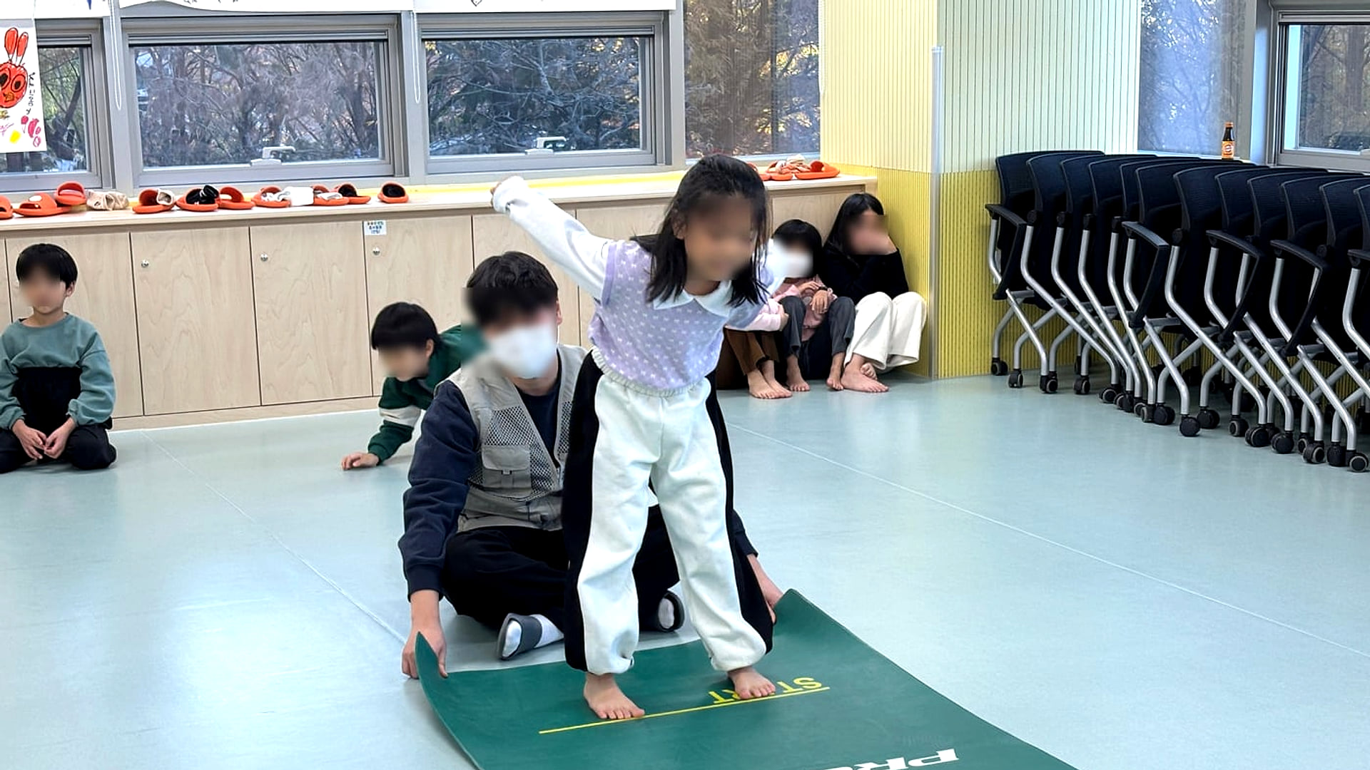 지도자가 곁에서 보조하는 가운데 매트 위에서 균형을 잡는 아이